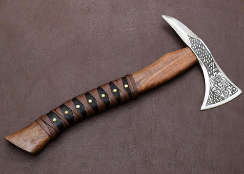 A handcrafted axe with a Corban steel blade and a Rose wood handle, featuring a decorative pattern on the blade and a leather cover.
