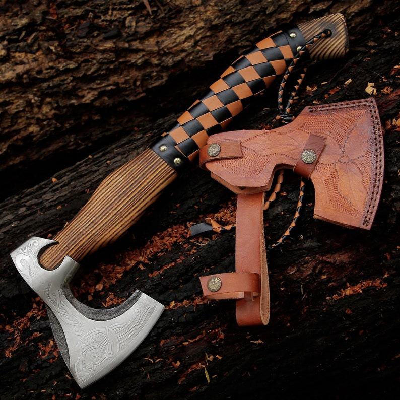 A steel camping axe with a brown and black leather cover, placed on a wooden surface.