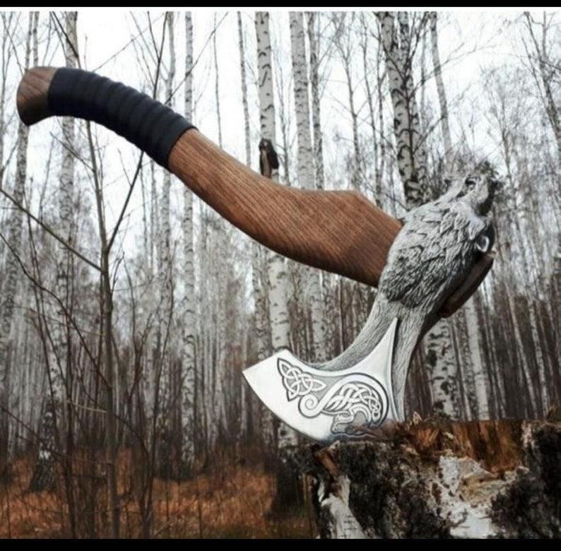 A handmade engraved axe with a leather cover, featuring a wooden handle and a steel head, placed upright in a forest environment.
