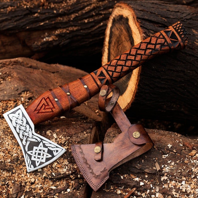 A handmade axe with a wood handle and Corban steel blade, featuring intricate engravings, accompanied by a handmade leather cover.