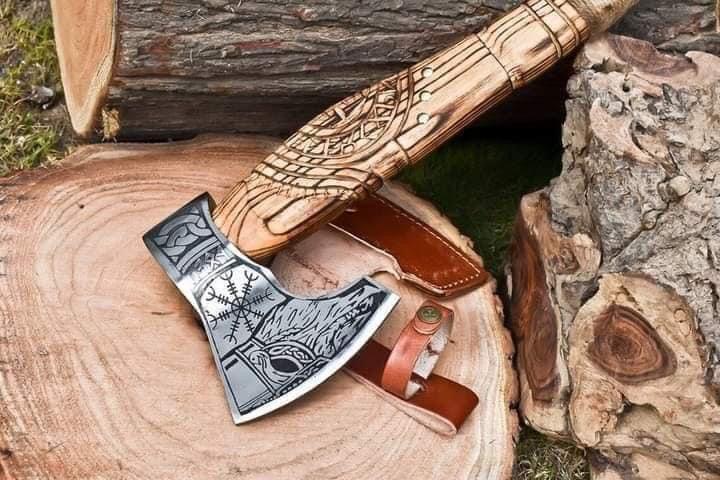 A handcrafted axe with a patterned headrest, sitting next to a wooden handle with a leather cover, placed on a natural wood setting.