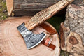 A handcrafted axe with a patterned headrest, sitting next to a wooden handle with a leather cover, placed on a natural wood setting.