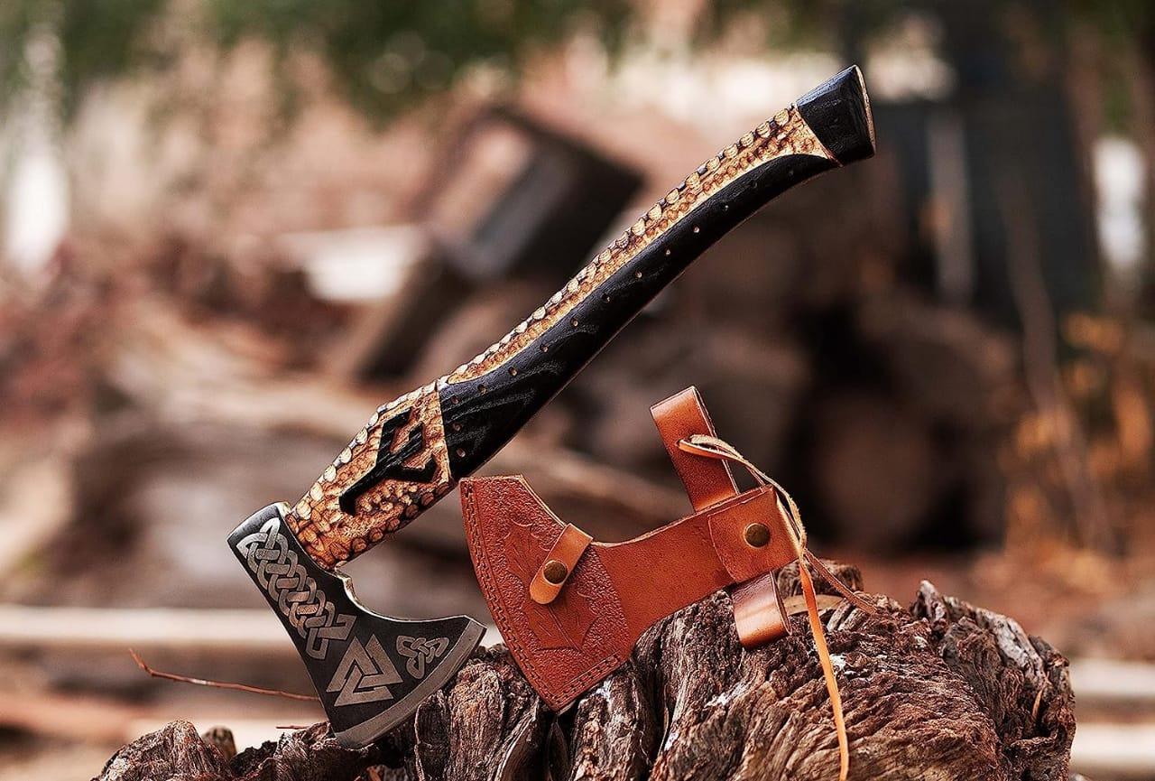 A Viking engraved axe with a black handle and a brown leather cover, placed on a wooden surface.