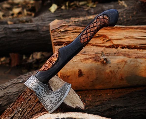 A handcrafted Viking axe with a detailed blade and a black and ash wood handle, resting against a wooden backdrop.