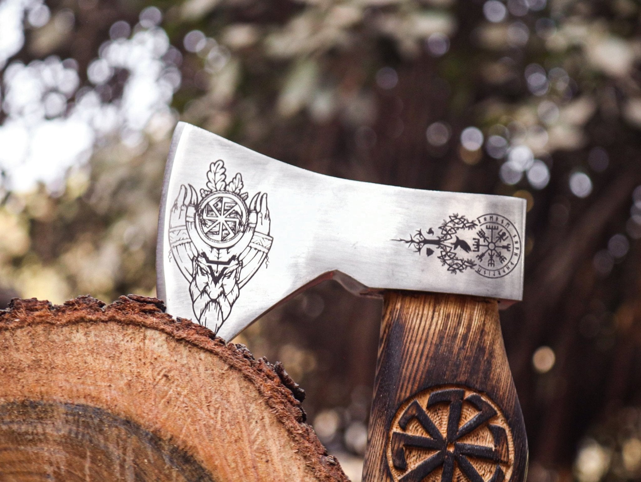 A corban steel axe with a decorative engraving on the blade and a wooden handle, placed against a natural outdoor background.