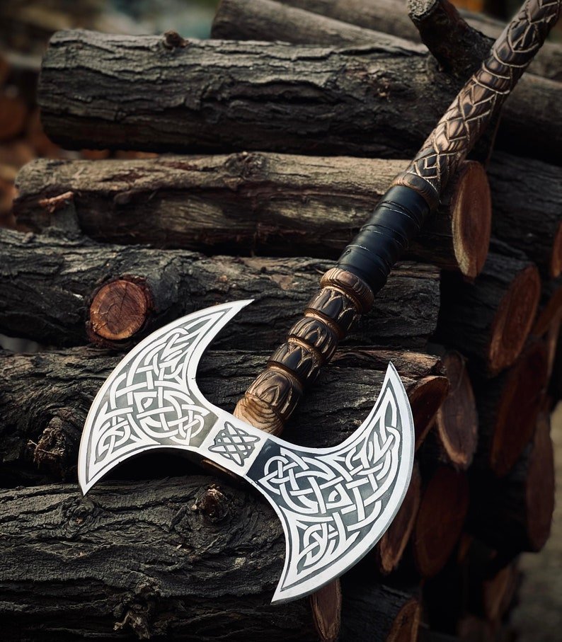 A handcrafted double bit axe with intricate engravings on the blade, featuring a wooden handle with leather wrapping and a carbon steel head.