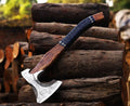 A steel axe with a patterned blade and a dark-colored wooden handle, leaning against a stack of logs.