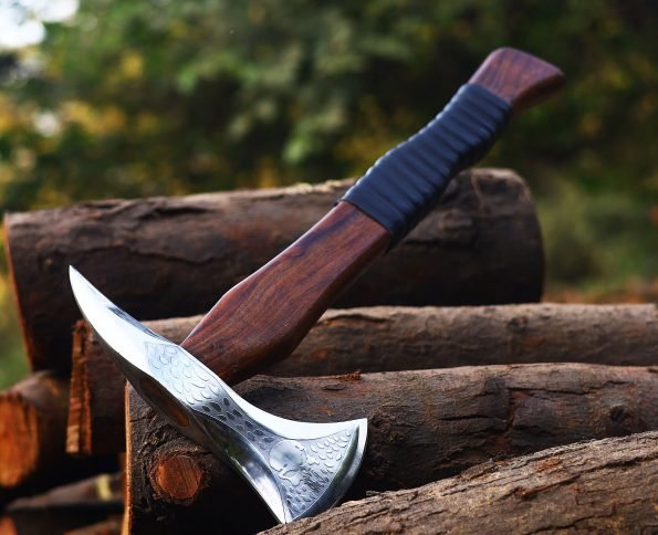 A personalized steel axe with a brown wooden handle and a leather cover, placed against a backdrop of wooden logs.