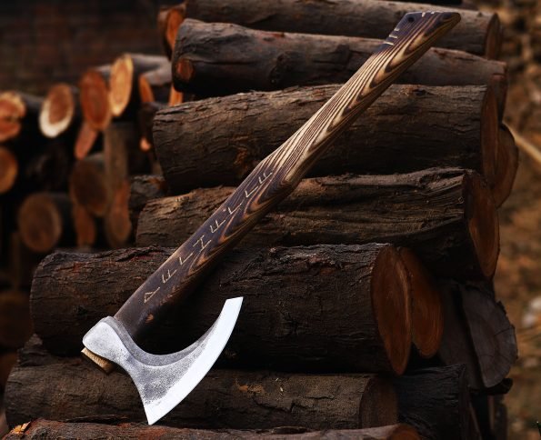 A Viking axe with a wooden handle and a metallic head resting on a stack of wooden logs.