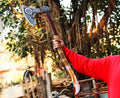 A person holding a Viking axe with a decorative pattern on the blade, featuring a brown wooden handle and a silver-colored head. A handmade leather cover is attached to the axe.