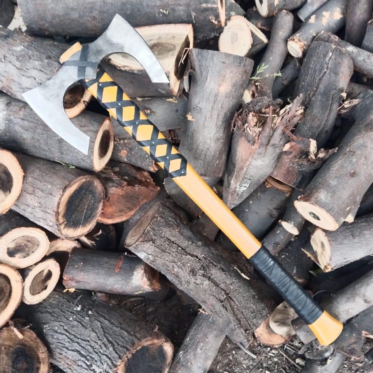 A double-headed axe with a yellow and black handle wrapped in leather, lying on a pile of wood.